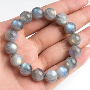 May include: A gray labradorite gemstone bracelet with iridescent blue and green hues. The bracelet is made of round beads and is strung on a clear elastic cord.