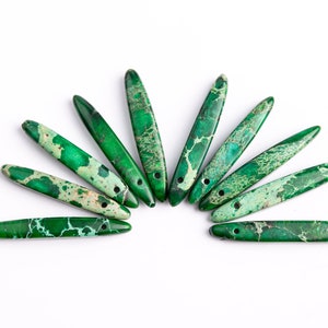 May include: Ten green and white marbled stone beads with a hole drilled through the center of each bead. The beads are arranged in a semi-circle.