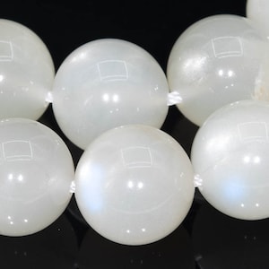 May include: A strand of white moonstone beads. The beads are round and smooth, with a subtle iridescent sheen.