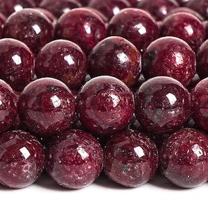 May include: A close-up of a strand of round, dark red gemstone beads. The beads are smooth and polished, with a slight sparkle.