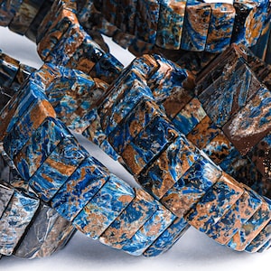Pode incluir: Um close-up de várias pulseiras feitas de contas de pedra com padrões azuis e marrons. As contas são retangulares e têm um aspecto marmorizado único.