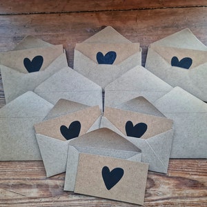 May include: A stack of brown paper envelopes with black heart designs. The envelopes are arranged in a pyramid shape, with the top envelope having a single heart design and the bottom envelope having a heart design on the front.