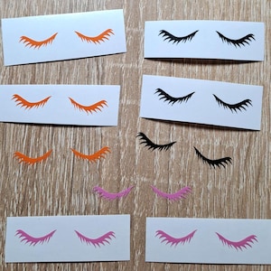 Pode incluir: Um conjunto de 10 adesivos de cílios em três cores: laranja, preto e rosa. Os adesivos estão em cartão branco.