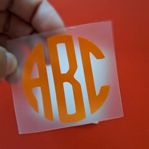 Könnte beinhalten: Eine transparente Folie aus Haftvinyl mit den Buchstaben "ABC" in leuchtend orange, die in einem Kreis angeordnet sind.