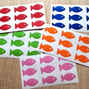 Puede incluir: Un conjunto de diez hojas de pegatinas de peces de colores. Cada hoja tiene 12 pegatinas de peces en una variedad de colores, incluyendo rojo, naranja, verde, azul y rosa.