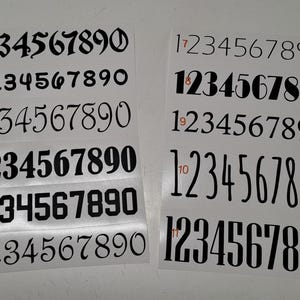 Peut inclure: Un ensemble de 11 feuilles blanches avec des chiffres noirs imprimés dessus. Les chiffres sont 1234567890 et sont dans différentes polices. Les feuilles sont numérotées de 1 à 11.