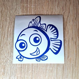 Puede incluir: Una pegatina de pez de dibujos animados azul con ojos grandes y una sonrisa. El pez tiene una aleta en la espalda y dos aletas a los lados.