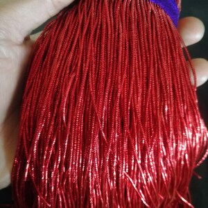 Puede incluir: Un manojo de cordones metálicos finos de color rojo. Los cordones están apretados y tienen un acabado brillante y reflectante.