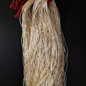 Puede incluir: Un haz de cordón metálico de color dorado atado con una cinta roja. El cordón está hecho de muchos hilos finos de alambre.