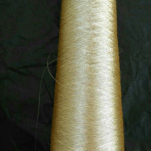 May include: A spool of gold metallic thread wound on a black bobbin.