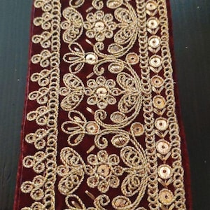 Peut inclure: Garniture en velours bordeaux avec broderie dorée et paillettes. La garniture présente un motif floral répétitif.