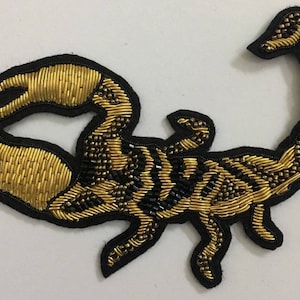 Op de afbeelding: Een geborduurde scorpion patch in goud en zwart. De scorpion is gedetailleerd met gouden draad en zwarte kralen.