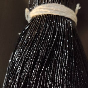 Op de afbeelding: Een close-up van een bundel zwarte metallic draad. De draad is strak gewikkeld en heeft een lichte glans.