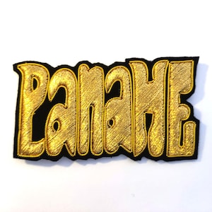 Peut inclure: Un patch brodé or avec le mot "PANAHE" dans une police stylisée sur un fond en feutre noir.