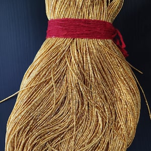 Può includere: Un rotolo di filo metallico dorato, legato con uno spago rosso. Il filo è avvolto strettamente e sembra essere fatto di piccole perline luccicanti.