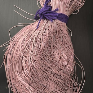 May include: A large bundle of thin, metallic rose gold wire gathered and secured in the centre with a thick, knotted purple yarn tie. The individual strands of wire are flexible and arranged in a loose, flowing cluster that fans out at the ends.