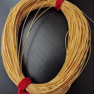 Peut inclure: Une bobine de fil de couleur or enveloppée de ficelle rouge. Le fil est fin et semble être en métal.