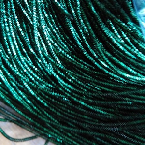 May include: A close-up of a spool of emerald green metallic thread. The thread is shiny and has a slight sparkle.