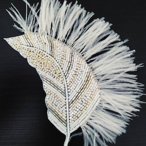 Peut inclure: Une garniture de plumes blanches avec un motif de feuille perlée. La feuille est faite de perles blanches et argentées et a une surface texturée.