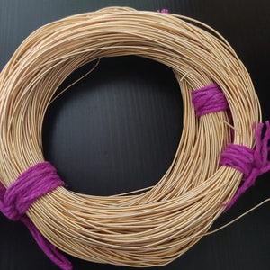 Peut inclure: Une bobine de fil de couleur or enveloppée de liens en tissu violet. Le fil est enroulé étroitement en cercle.