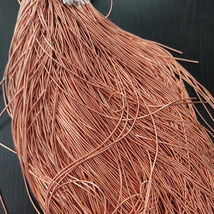 Peut inclure: Un gros paquet de fil de cuivre, enroulé serré et disposé en une forme lâche et fluide. Le fil est de couleur brun rougeâtre chaud et semble être de très faible calibre.