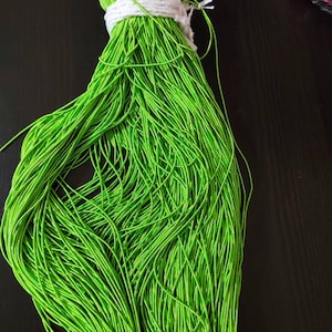 May include: A bundle of bright green elastic cord, tied together with white string. The cord is tightly wound and appears to be made of a thin, stretchy material.