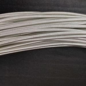 Peut inclure: Gros plan sur un paquet de cordes de guitare argentées. Les cordes sont enroulées et ont une finition brillante.