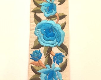 Trenza bordada flores de primavera de color azul pastel sobre fondo crudo