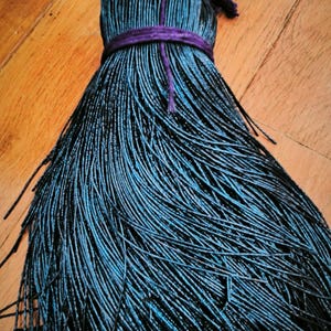 Może przedstawiać: Czarno-niebieski frędzl z koralików z przewiązaną na górze fioletową wstążką.