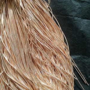 Puede incluir: Primer plano de un haz de alambre de color dorado. El alambre está dispuesto de forma ordenada y organizada, con los extremos del alambre sobresaliendo.