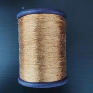 Op de afbeelding: Een spoel met gouden metallic draad met een donkerblauwe plastic spoel.