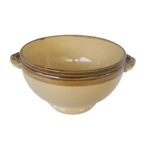 May include: A ceramic bowl with a light yellow interior and exterior, featuring a brown band around the middle and two small handles. The bowl has a rounded shape and sits on a small base. The overall design is simple and classic.