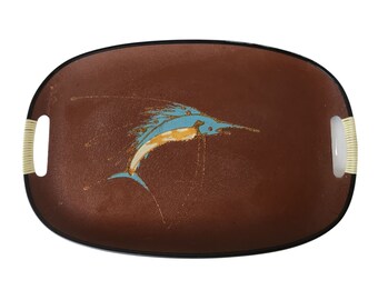 May include: Oval serving tray with a brown surface and a black rim. The tray features a blue and yellow marlin design. The handles are made of woven beige material. A decorative piece for serving food and drinks.