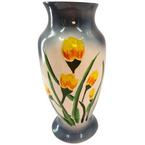 Może przedstawiać: Ceramiczny wazon z rozszerzoną górą i podstawą, pomalowany żółtymi i pomarańczowymi kwiatami oraz zielonymi liśćmi. Wazon ma gradient niebieskiego i szarego na górze i na dole, ze środkiem w kolorze kremowym. Wazon ma około 20 cm wysokości.