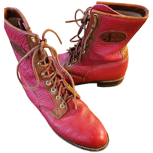 May include: Red leather boots with brown detailing and laces. The boots have a textured finish and the brand name "Justin" is visible. The boots are designed with a lace-up closure and a sturdy sole. The boots are suitable for various outdoor activities.