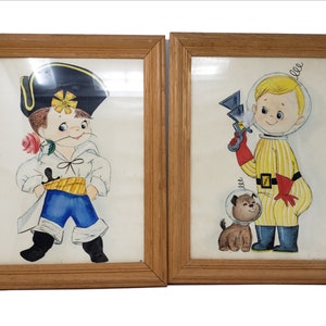 Könnte beinhalten: Zwei gerahmte Vintage-Drucke. Einer zeigt einen Cartoon-Jungen in einem Kostüm, der eine Rose hält, der andere einen Jungen in einem Raumanzug mit einer Strahlenkanone und einem Hund mit einem Weltraumhelm. Beide sind in Holzrahmen.