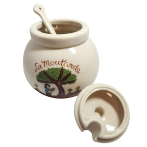 May include: Cream ceramic mustard pot with lid and spoon. The pot has a tree illustration and the words "La moutarde". The lid is off to the side. The spoon is inside the pot.
