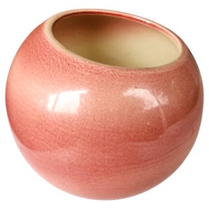 May include: A spherical ceramic vase with a glossy, mottled pink exterior finish and a smooth, cream-colored interior. The vase features a wide, circular opening at the top, angled slightly to one side, showcasing a simple, rounded, and bulbous form.