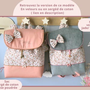 May include: Two backpacks with flap closures and decorative bows. The left backpack is solid dusty pink with a floral print panel. The right backpack is grey corduroy with a floral print panel. Both feature drawstring closures and small bows.