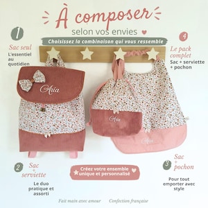 May include: A dusty rose corduroy backpack, a drawstring pouch, and a bib, all featuring a floral print and the name Aria embroidered in white. The items are displayed on a wooden wall hook rack with star-shaped pegs, accompanied by French text.