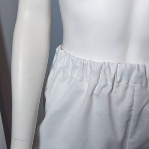 May include: A pair of plain white bloomers featuring an elasticized waistband with gathered fabric detailing. The garment is displayed on a mannequin, showing a simple, solid white design with a soft texture and a comfortable, loose-fitting silhouette.