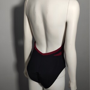 May include: Black leotard with a burgundy trim and a halter neckline. The leotard has a low back and is designed for dance or gymnastics.