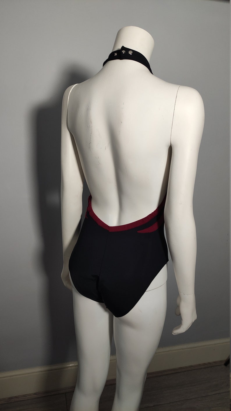 May include: Black leotard with a burgundy trim and a halter neckline. The leotard has a low back and is designed for dance or gymnastics.