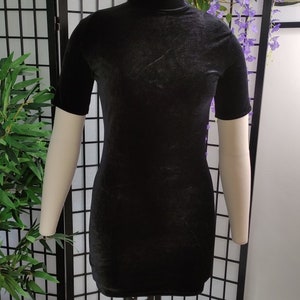 Puede incluir: Un minivestido negro de terciopelo con mangas cortas y cuello alto. El vestido se exhibe en un maniqu&iacute;. El vestido es de color negro liso y tiene un aspecto suave y texturizado. El vestido es de estilo ajustado.