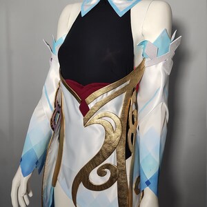 May include: A white and blue cosplay costume with gold accents. The costume features a black top, a white skirt with a blue and white pattern, and gold trim. The costume is worn on a mannequin.