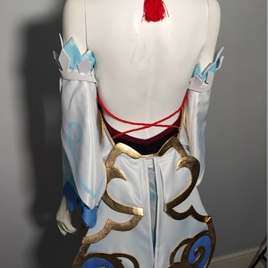 May include: White and blue cosplay costume with gold and blue accents. The costume features a red tassel and a red string tie in the back.