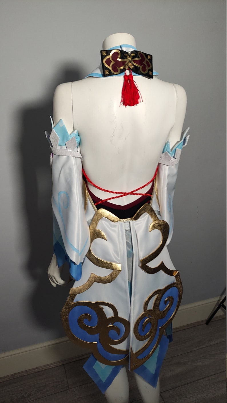 May include: White and blue cosplay costume with gold and blue accents. The costume features a red tassel and a red string tie in the back.