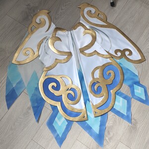 May include: A white fabric costume piece with blue and gold accents. The fabric has a cloud and diamond pattern. The piece is designed to look like wings.