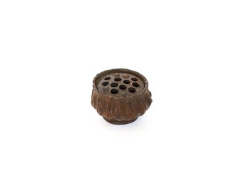 May include: A small, brown, metal flower frog with a circular top and a scalloped base. The top has a series of holes for holding flowers.