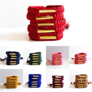 May include: A set of 10 colorful friendship bracelets with gold metal accents. The bracelets are stacked in a pile, with each bracelet featuring a different color. The colors include red, navy blue, green, pink, yellow, blue, burgundy, and orange.